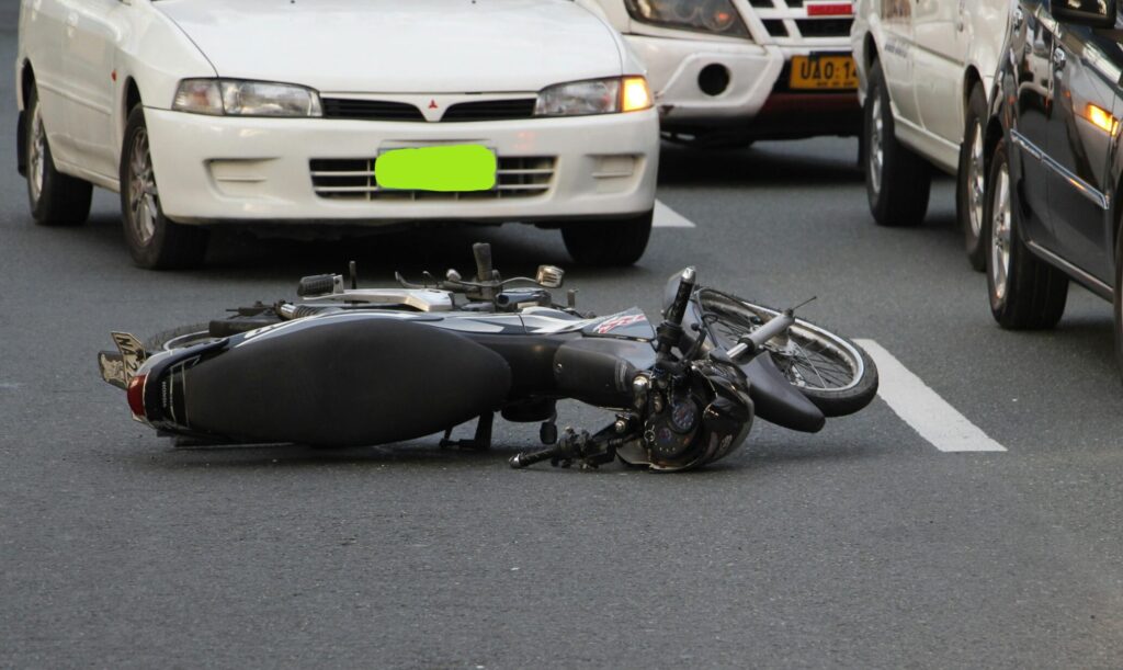 A motorcycle lies on a city road amidst traffic, indicating a recent accident.