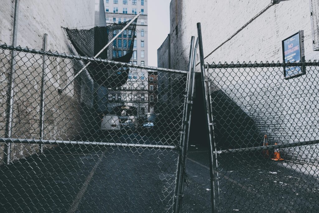 Chain link fenced urban alleyway with warning signs, conveying a sense of security and confinement.